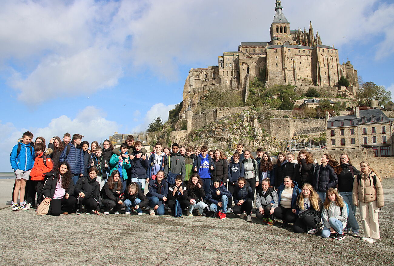 Schülerinnen und Schüler posieren für ein Gruppenfoto vor Le Mont-Saint-Michel